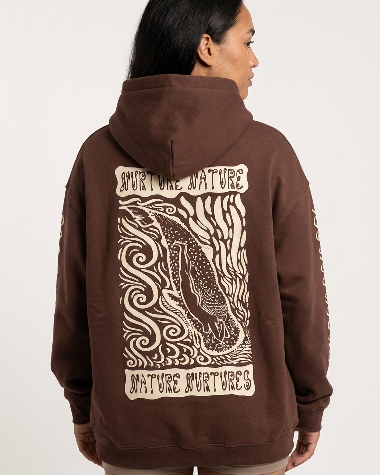 Person wearing a brown hoodie with a woman and whale ocean inspired graphic design on the back against a white background
