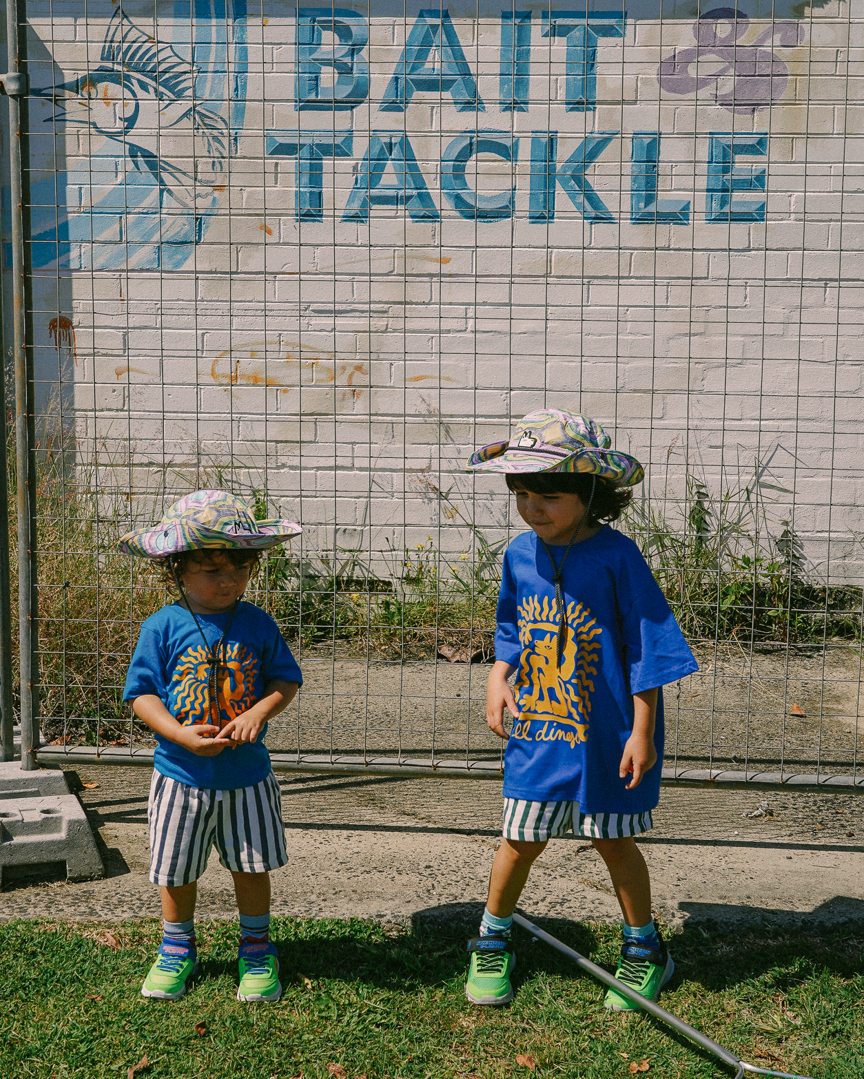 Two children in blue shirts and hats standing in front of a 'Bait & Tackle' sign.