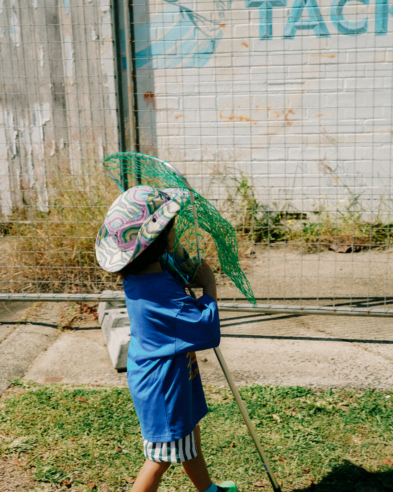 kid wearing colourful hat holding a fishing net against a wall with graffiti.