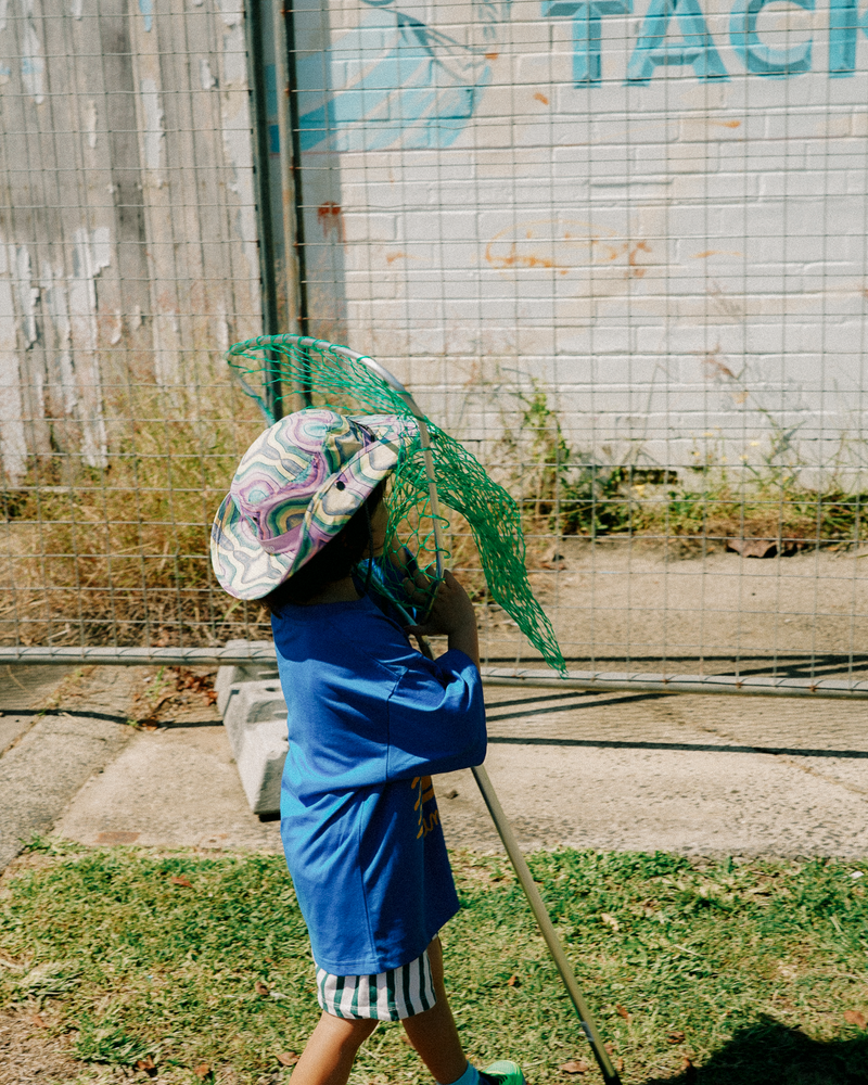 kid wearing colourful hat holding a fishing net against a wall with graffiti.