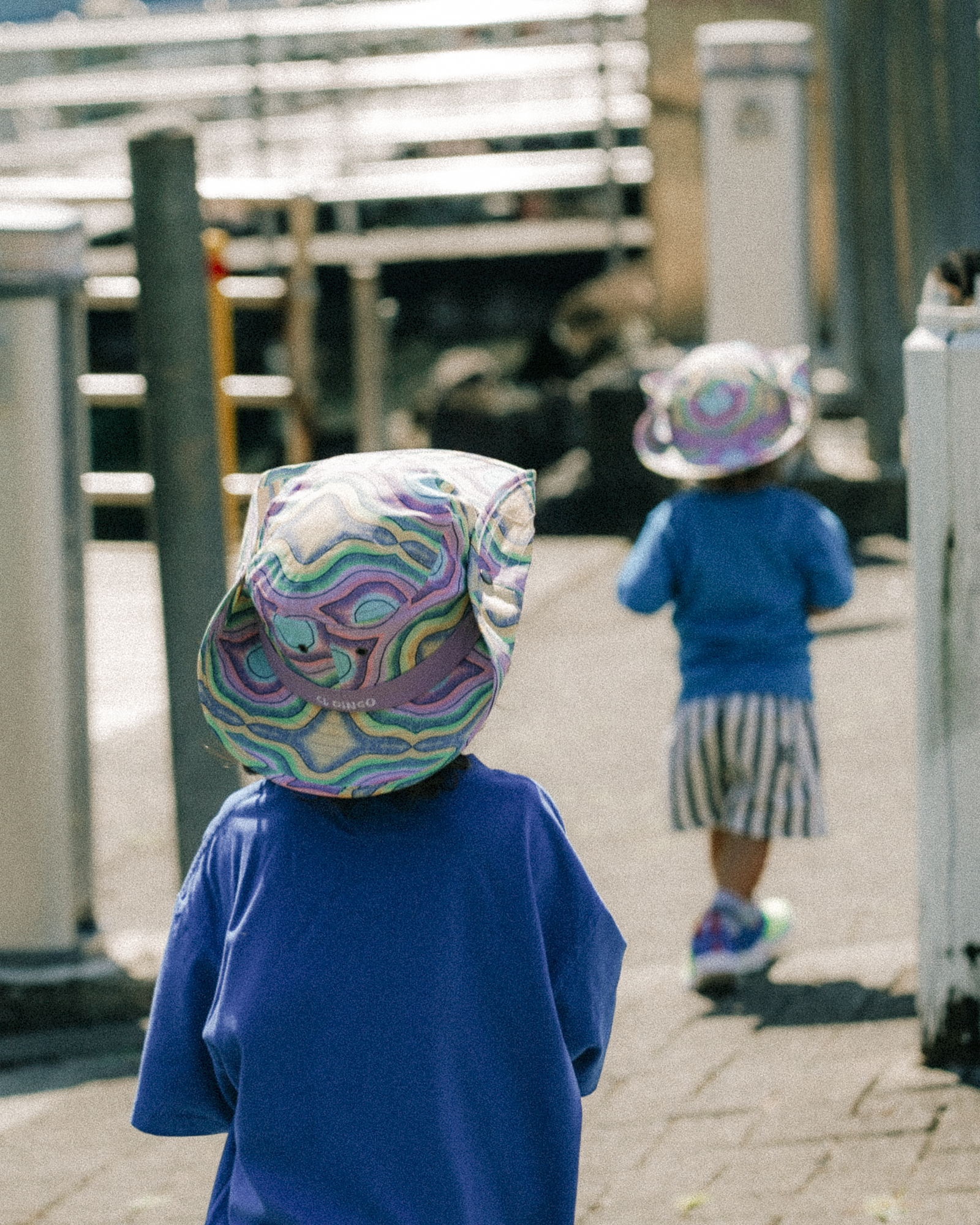 Two children wearing colorful hats on a paved walkway.