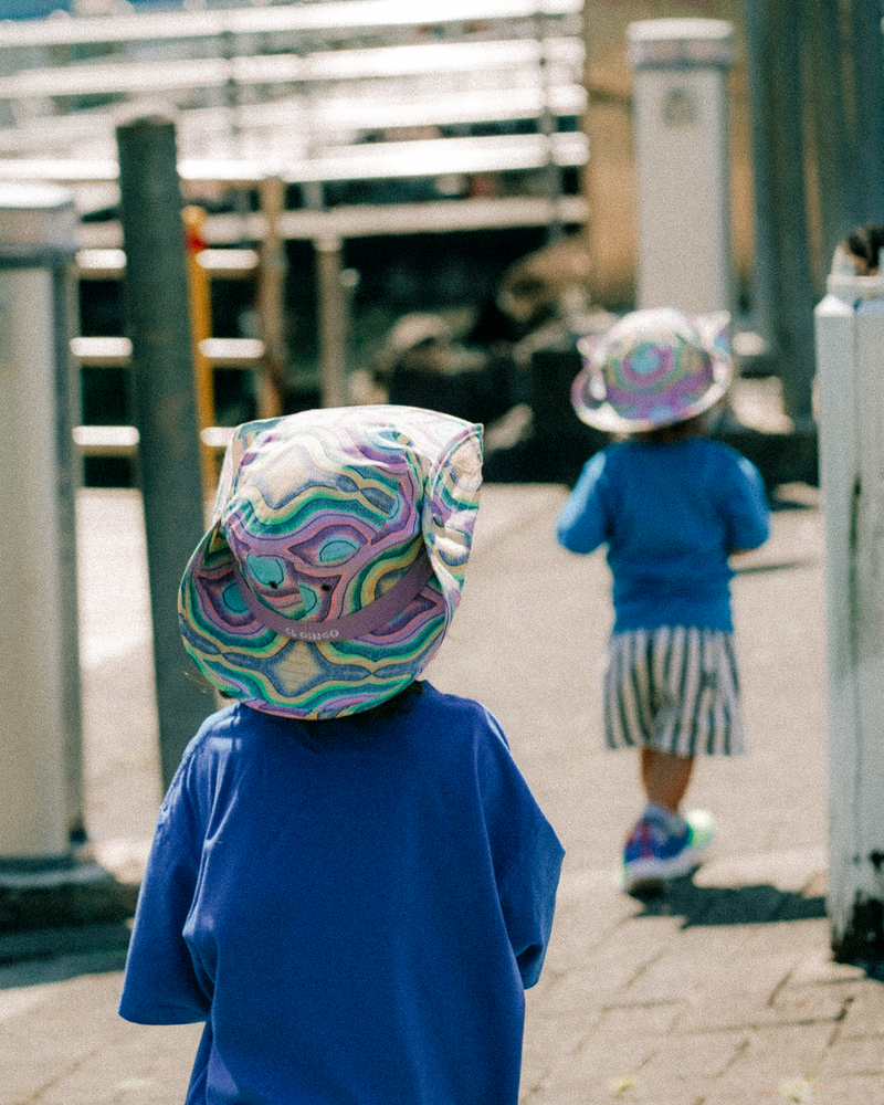 Two children wearing colorful hats on a paved walkway.