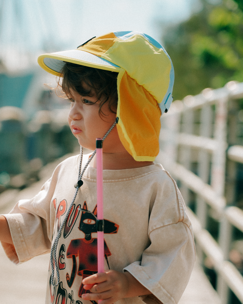 Child wearing a blue and yellow cap with a neck flap against a neutral background