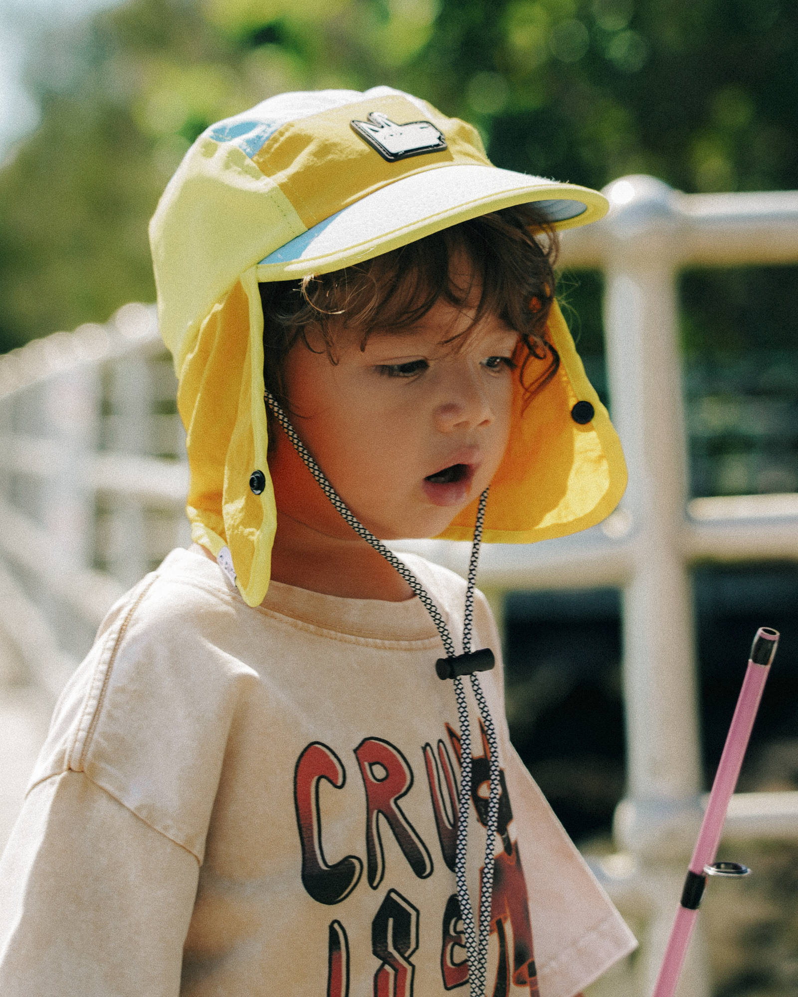 Child wearing a yellow sun hat with a chin strap, standing outdoors.