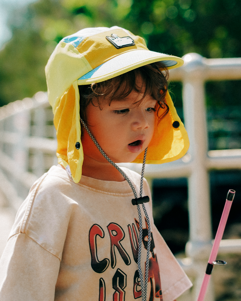 Child wearing a yellow sun hat with a chin strap, standing outdoors.