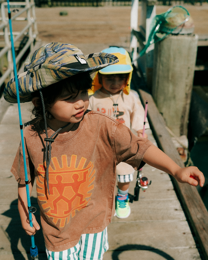 Two children on a wooden dock with fishing equipment wearing cool kids sun hats