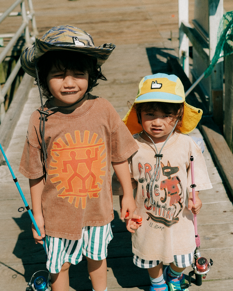 Two children on a wooden dock holding fishing rods, wearing sun safe sun hats and casual clothing.